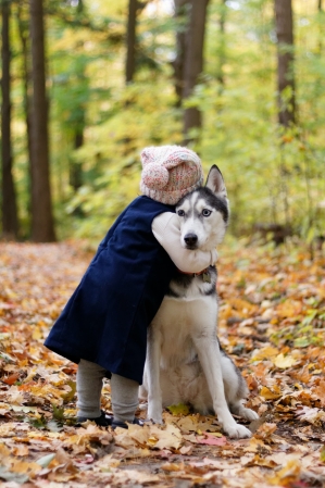 a child hugging a husky dog in a forest
